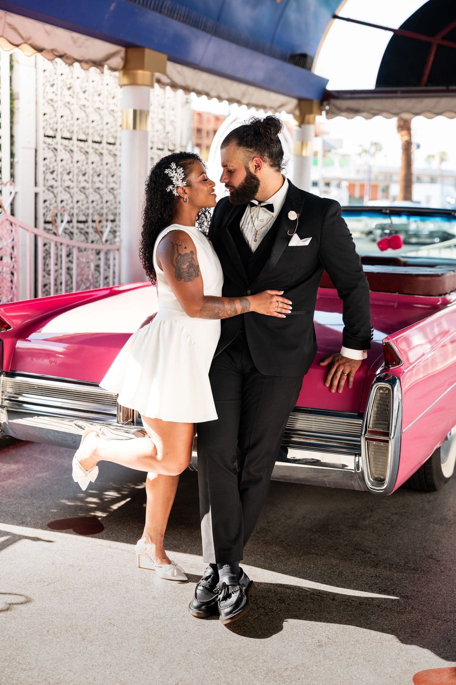 A couple poses against a pink classic car at a retro venue