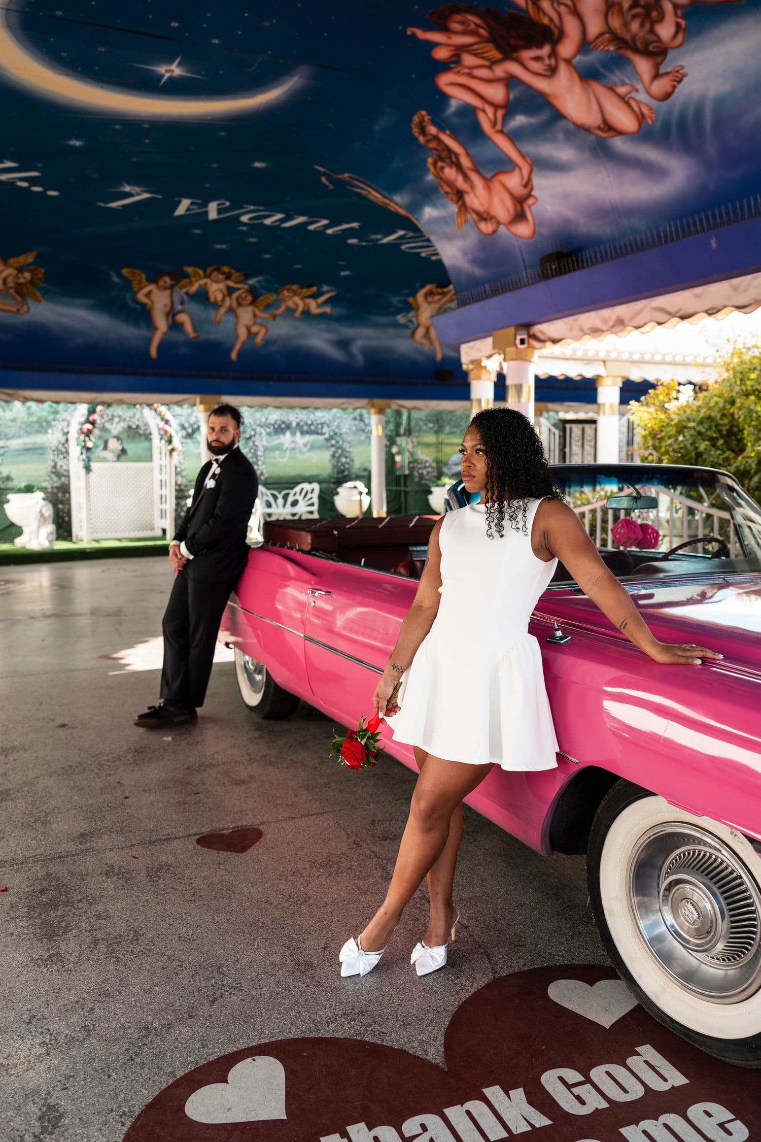 Romantic poses beside a pink classic car under blue skies