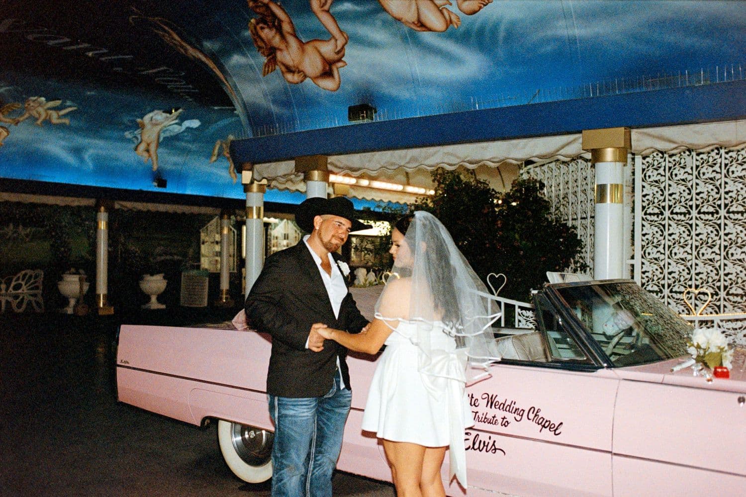 A couple celebrating near a vintage pink Cadillac