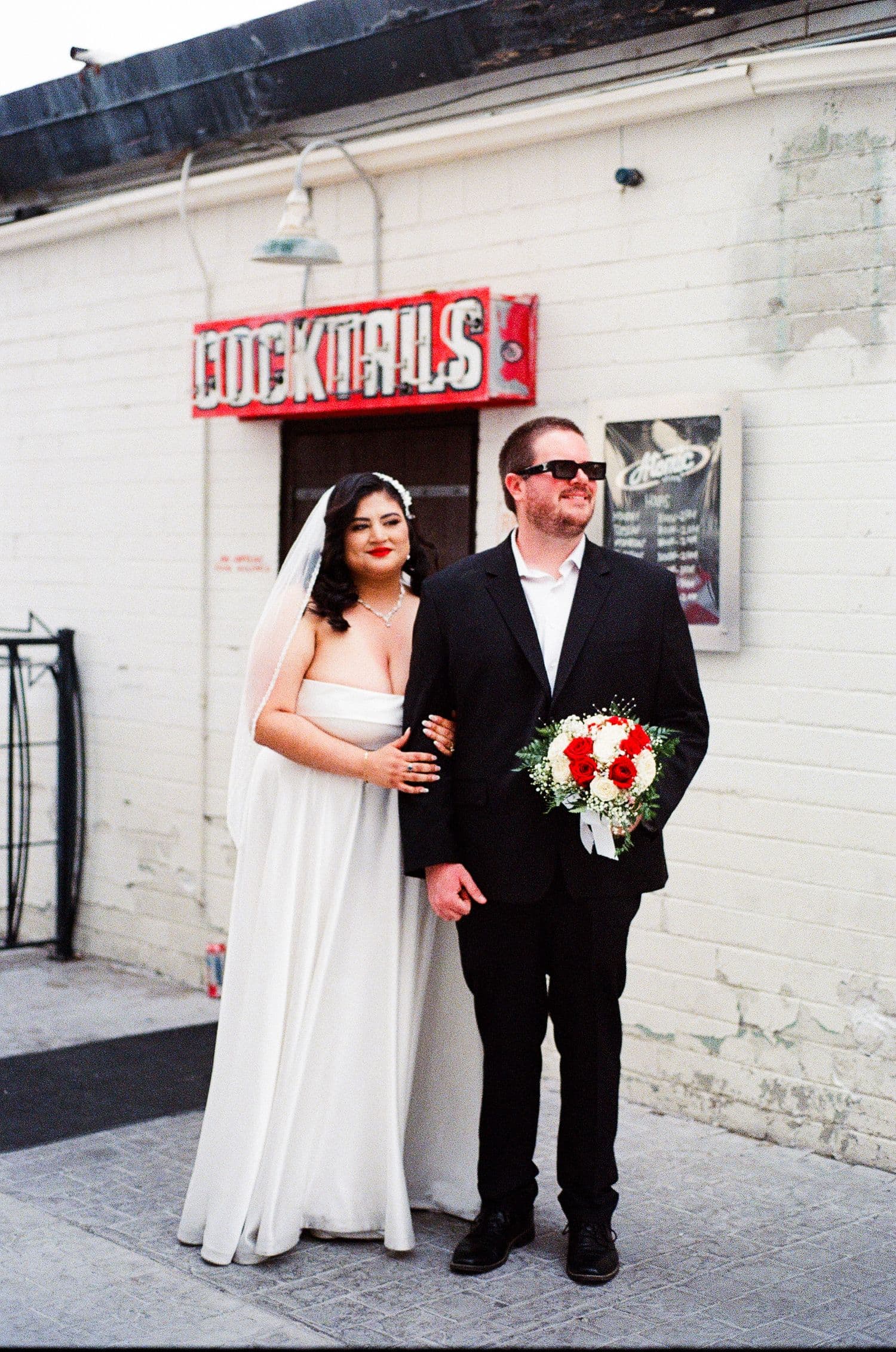A couple outside a venue with a red neon sign and white brick wall